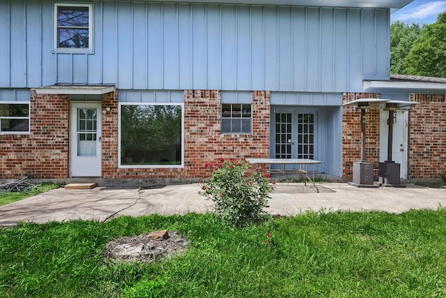 doorway to property featuring a patio area, board and batten siding, brick siding, and french doors