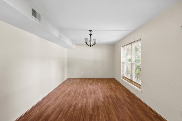 empty room with wood finished floors and a chandelier
