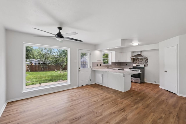 kitchen with stainless steel gas stove, wall chimney range hood, a peninsula, white cabinetry, and a sink