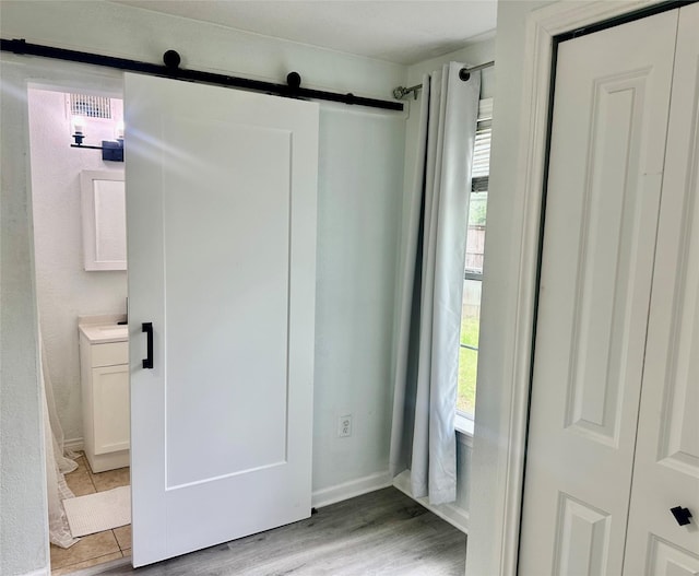 3024 Carnation Ave, Fort Worth, TX 76111 - unfurnished bedroom with a barn door, light wood-style floors, and baseboards