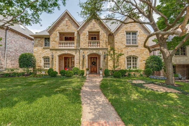 view of front of property with a balcony, a front lawn, and stone siding
