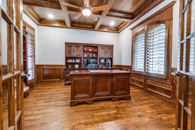 office space with a wainscoted wall, wood finished floors, ornamental molding, a ceiling fan, and coffered ceiling