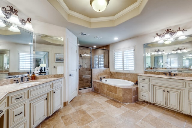 bathroom featuring a tray ceiling, a garden tub, a shower stall, ornamental molding, and two vanities