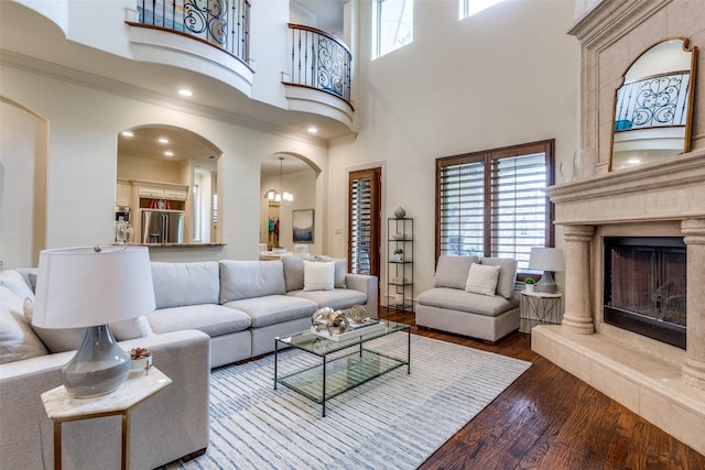 living area featuring arched walkways, a towering ceiling, wood finished floors, a high end fireplace, and ornamental molding