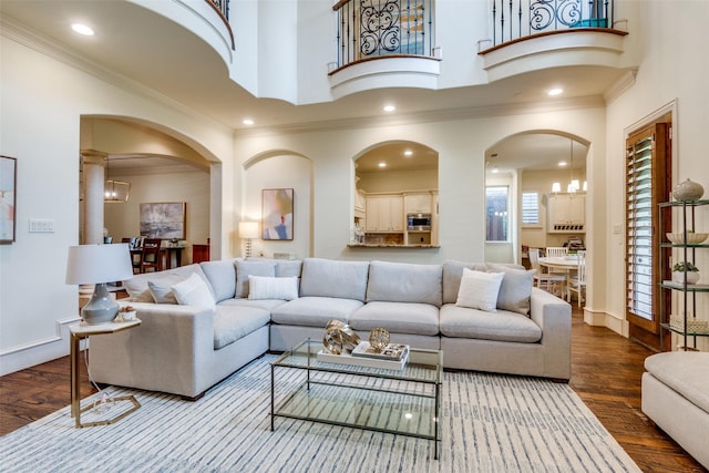 living room featuring a chandelier, ornamental molding, wood finished floors, arched walkways, and baseboards