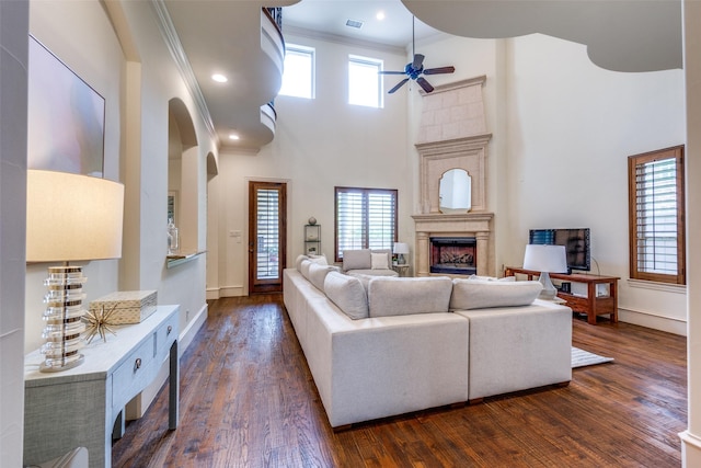 living area with a towering ceiling, a ceiling fan, a fireplace, dark wood-style flooring, and baseboards