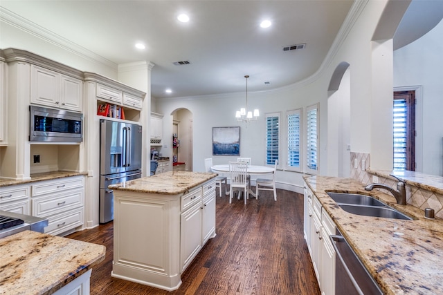 kitchen featuring appliances with stainless steel finishes, arched walkways, a sink, light stone counters, and a chandelier