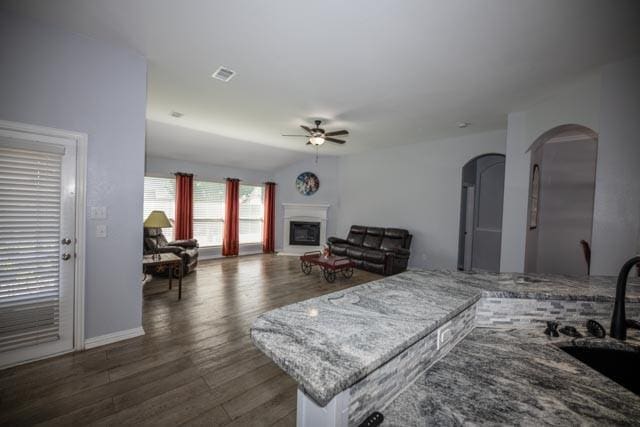 107 Harvest Way, Crandall, TX 75114 - living area featuring a ceiling fan, arched walkways, dark wood-style flooring, a fireplace with raised hearth, and baseboards