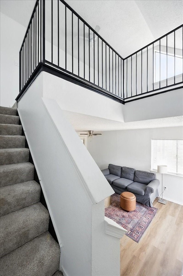 stairs featuring wood finished floors, a towering ceiling, and ceiling fan
