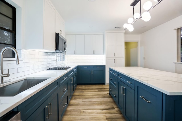 kitchen with a sink, blue cabinets, white cabinets, and appliances with stainless steel finishes
