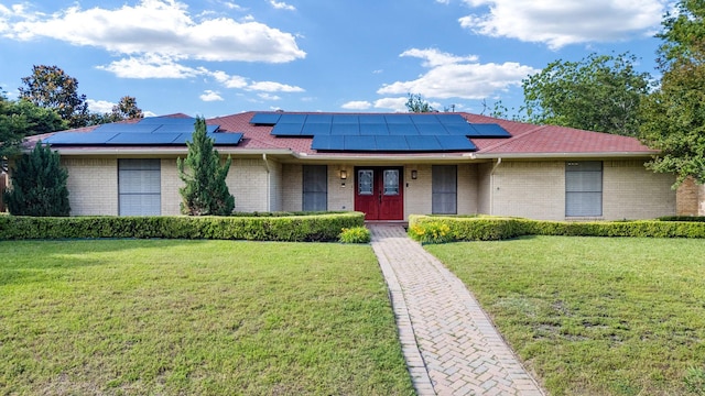 view of front of home with brick siding, a front yard, and roof mounted solar panels