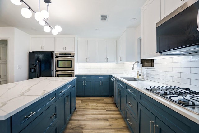 kitchen with appliances with stainless steel finishes, a sink, blue cabinets, white cabinets, and light wood finished floors
