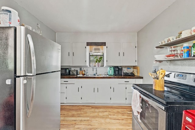 685 S First Ave, Stephenville, TX 76401 - kitchen featuring stainless steel appliances, a sink, light wood-type flooring, dark countertops, and white cabinetry