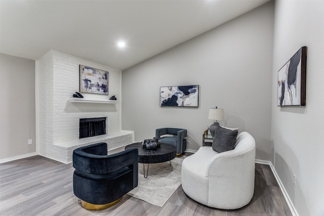 living room with lofted ceiling, wood finished floors, baseboards, a brick fireplace, and recessed lighting
