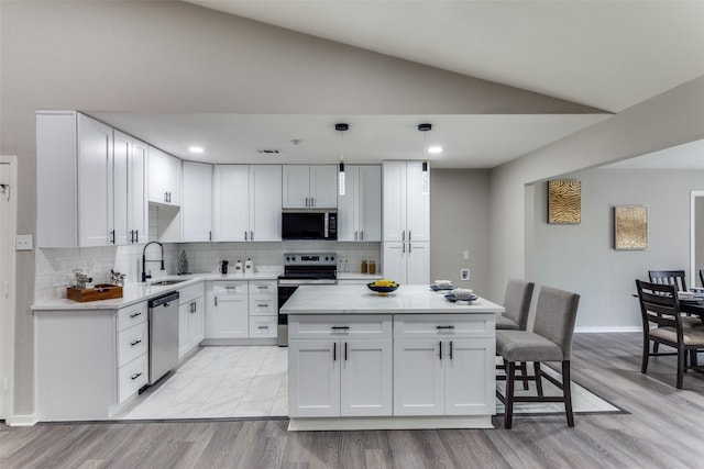 kitchen featuring appliances with stainless steel finishes, a sink, lofted ceiling, white cabinets, and a center island