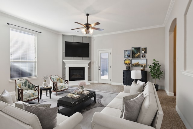 689 Barringer Ct, Fate, TX 75087 - carpeted living area featuring a ceiling fan, arched walkways, crown molding, baseboards, and a glass covered fireplace