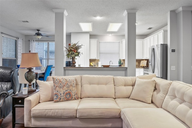 living room with a ceiling fan, a textured ceiling, and a skylight