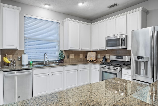 kitchen featuring appliances with stainless steel finishes, a sink, white cabinetry, tasteful backsplash, and a textured ceiling