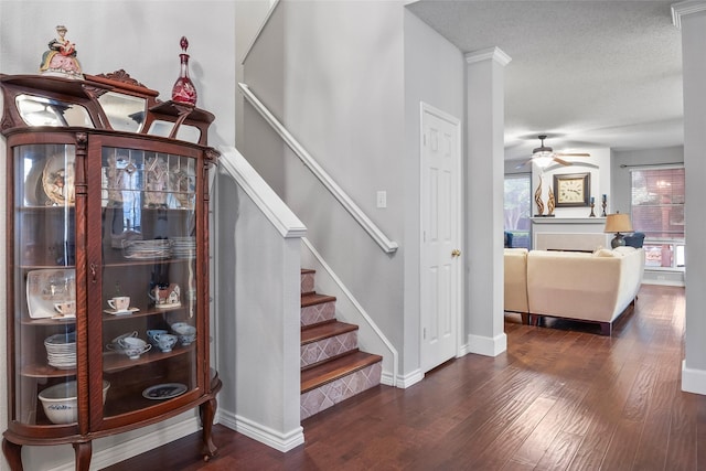 staircase featuring wood finished floors, ceiling fan, baseboards, and a textured ceiling
