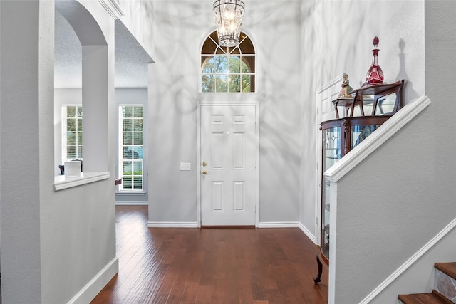 entrance foyer featuring wood finished floors, arched walkways, baseboards, a chandelier, and stairs