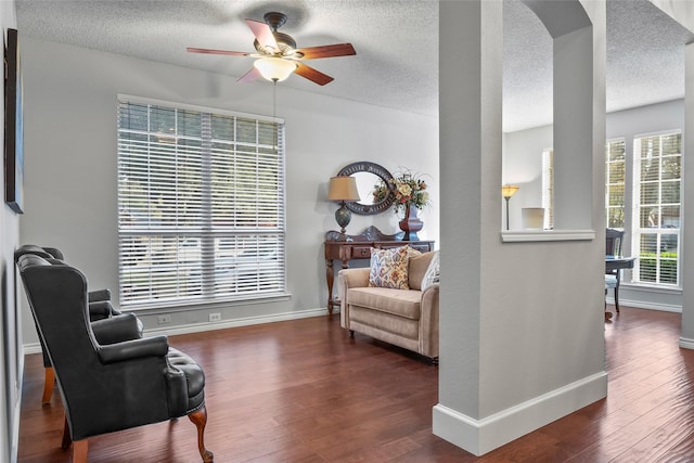 living area with ceiling fan, arched walkways, baseboards, wood finished floors, and a textured ceiling
