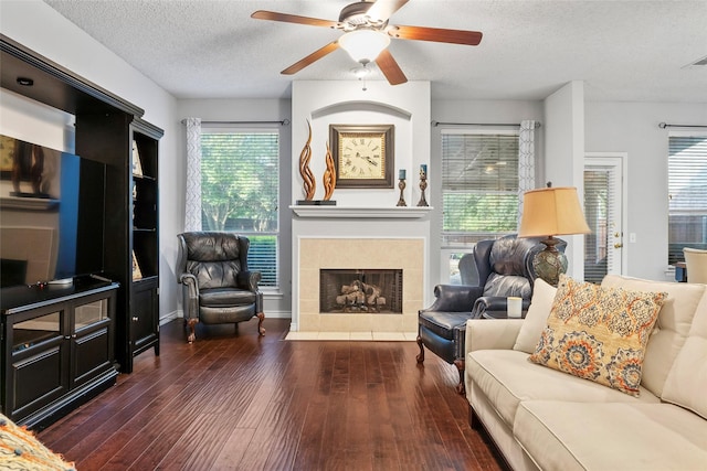 living room featuring a textured ceiling, hardwood / wood-style flooring, plenty of natural light, a tile fireplace, and a ceiling fan