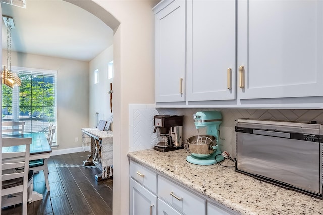 208 Johnson St, Granbury, TX 76048 - kitchen with arched walkways, decorative backsplash, light stone countertops, baseboards, and wood finish floors