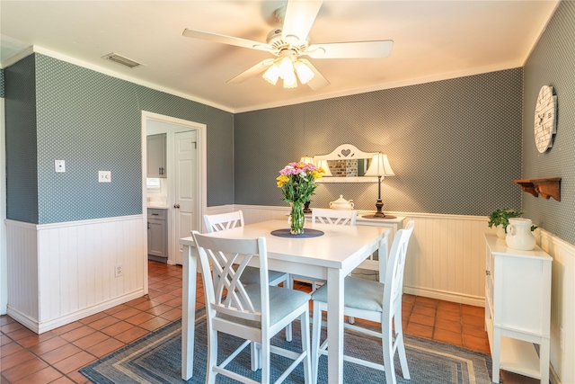 tiled dining area featuring a wainscoted wall and ceiling fan