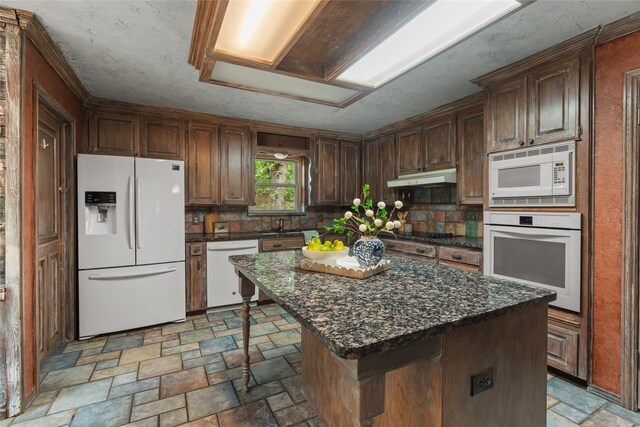 kitchen with white appliances, light stone finish flooring, tasteful backsplash, under cabinet range hood, and a center island