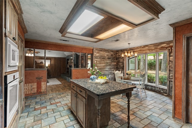 kitchen featuring white appliances, a chandelier, hanging light fixtures, light stone finish flooring, and a center island