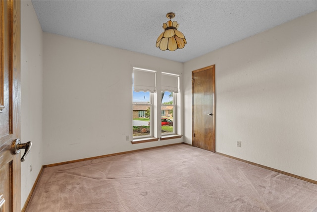 empty room with light colored carpet, baseboards, and a textured ceiling