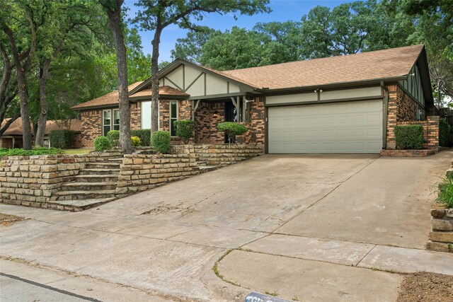 tudor house with brick siding, concrete driveway, a garage, and roof with shingles