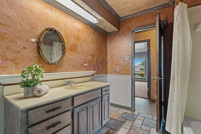 full bath featuring stone tile flooring, crown molding, wainscoting, and vanity