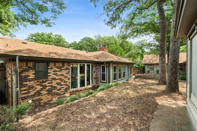 rear view of property with a chimney, roof with shingles, fence, and brick siding