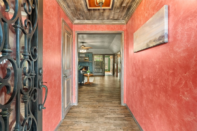 corridor featuring wood finished floors, a textured wall, vaulted ceiling, and crown molding