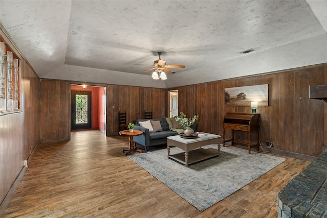 living area featuring wood-type flooring, ceiling fan, wooden walls, vaulted ceiling, and baseboards