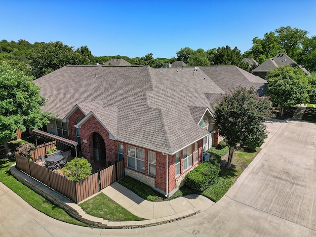 view of front of home with brick siding, a shingled roof, and fence
