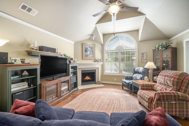living room with a ceiling fan, wood finished floors, a tiled fireplace, vaulted ceiling, and baseboards