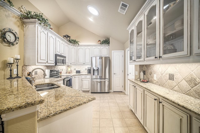 kitchen featuring appliances with stainless steel finishes, a sink, vaulted ceiling, light stone countertops, and a peninsula
