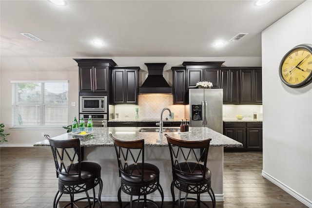 307 Acadia Ln, Forney, TX 75126 - kitchen with custom range hood, appliances with stainless steel finishes, an island with sink, dark wood finished floors, and a kitchen bar