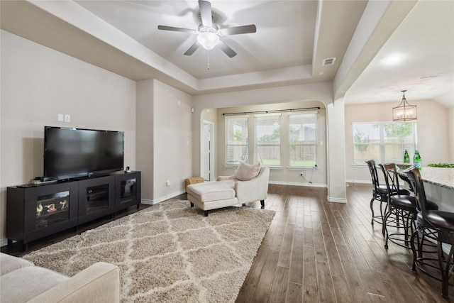 307 Acadia Ln, Forney, TX 75126 - living area with dark wood-style flooring, ceiling fan, baseboards, a tray ceiling, and arched walkways