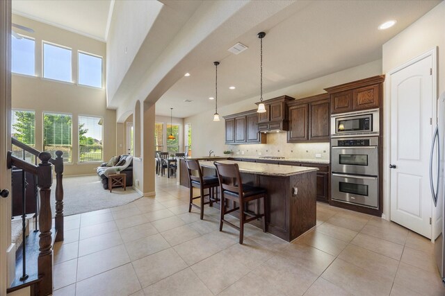 211 Crestbrook Dr, Rockwall, TX 75087 - kitchen with stainless steel appliances, arched walkways, a kitchen island with sink, a breakfast bar, and under cabinet range hood