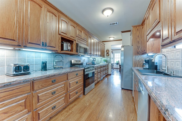 4402 Running Brook Dr, Rowlett, TX 75088 - kitchen featuring appliances with stainless steel finishes, a sink, decorative backsplash, light wood finished floors, and light stone counters