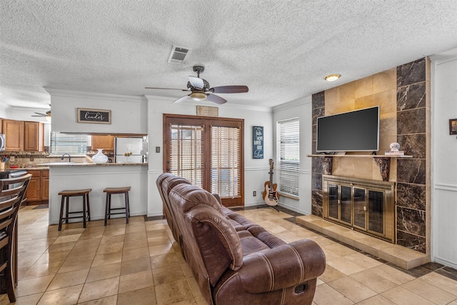 1104 Harwell Dr Unit 1514, Arlington, TX 76011 - living area featuring a ceiling fan, crown molding, a tiled fireplace, a textured ceiling, and light tile patterned floors