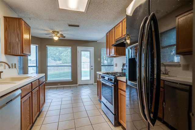kitchen featuring appliances with stainless steel finishes, a sink, brown cabinets, a ceiling fan, and a textured ceiling