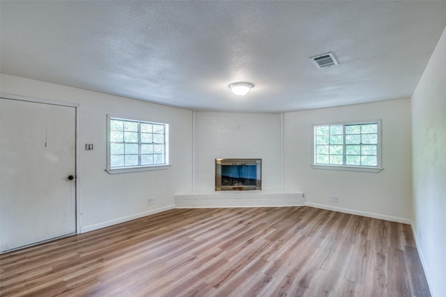 1104 Cortez St, Denison, TX 75020 - unfurnished living room featuring wood finished floors, healthy amount of natural light, a large fireplace, a textured ceiling, and baseboards