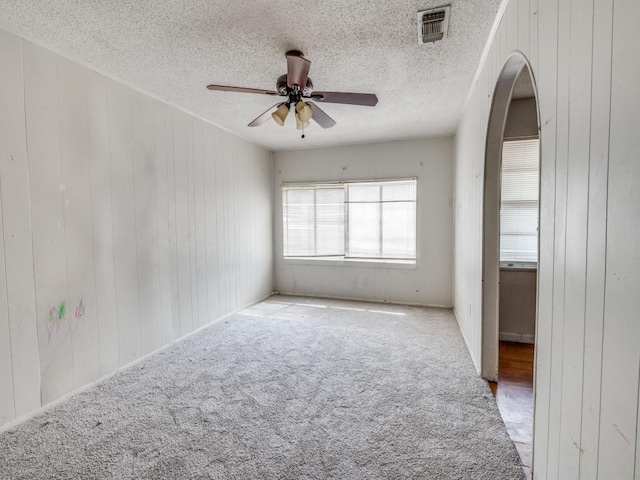 2203 Gould Ave, Fort Worth, TX 76164 - empty room featuring ceiling fan, carpet flooring, a textured ceiling, arched walkways, and wooden walls