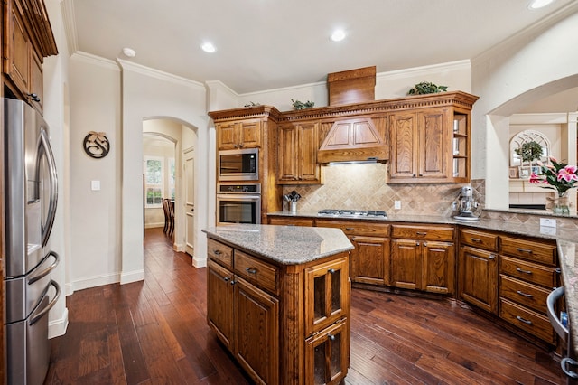 4651 Liam Dr, Frisco, TX 75034 - kitchen featuring appliances with stainless steel finishes, arched walkways, brown cabinetry, backsplash, and dark wood-type flooring