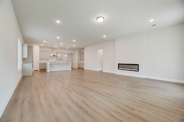 7113 El Matador Dr, Rowlett, TX 75088 - unfurnished living room with recessed lighting, light wood-style floors, a glass covered fireplace, and baseboards