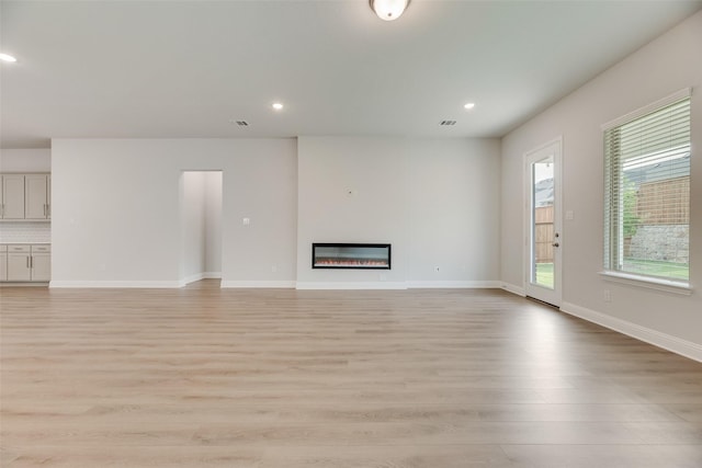7113 El Matador Dr, Rowlett, TX 75088 - unfurnished living room with light wood-style flooring, recessed lighting, a glass covered fireplace, and baseboards